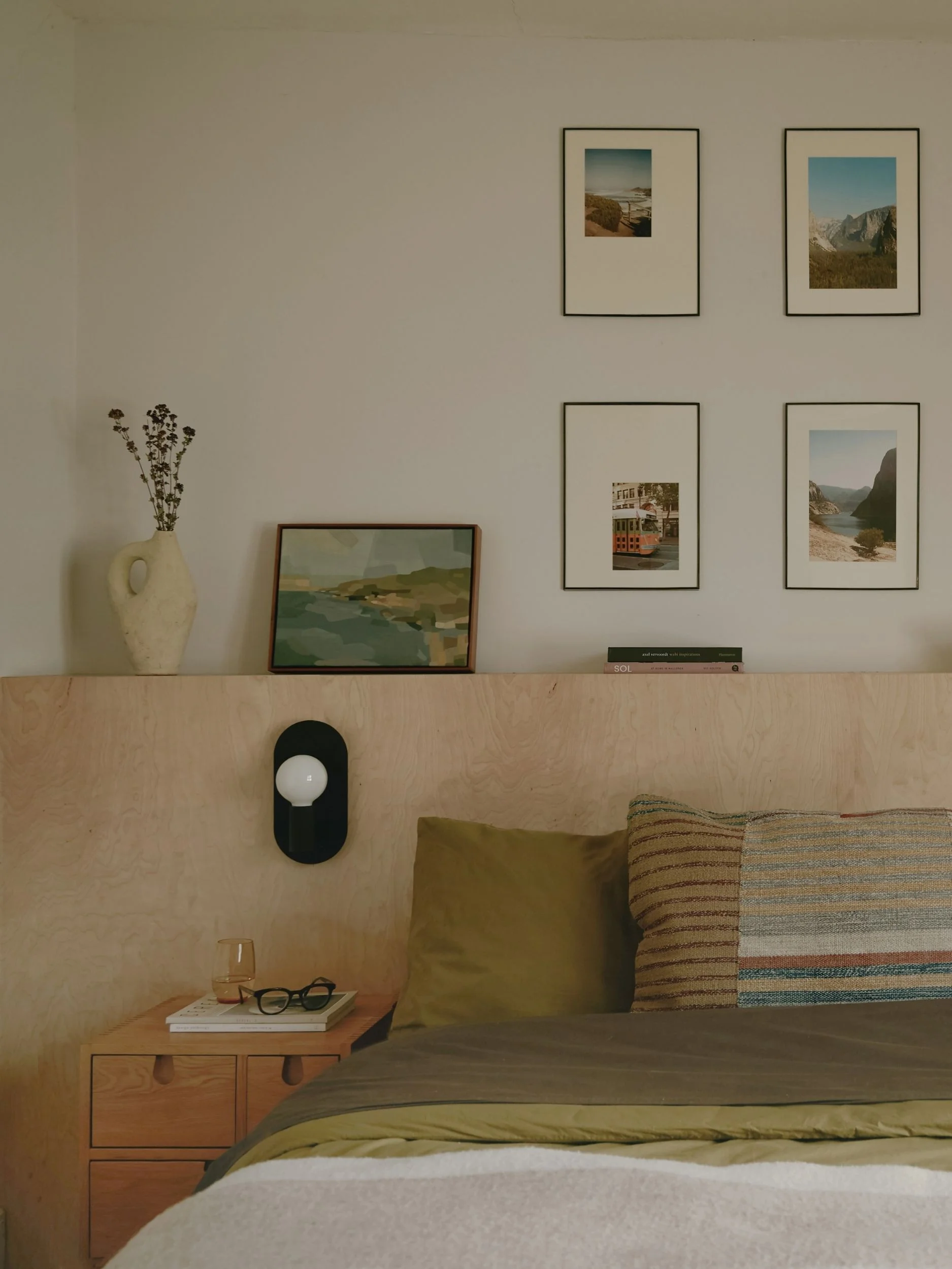 a bedroom with a plywood headboard and family photos on the wall behind, with green bedding on the bed