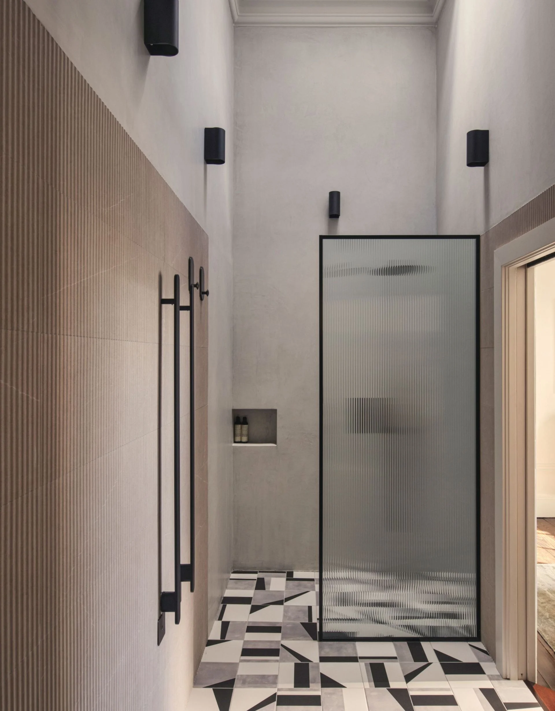 Bathroom with black, white and grey geometric tiled floor, fluted beige tile walls, black downlights and ribbed glass shower screen