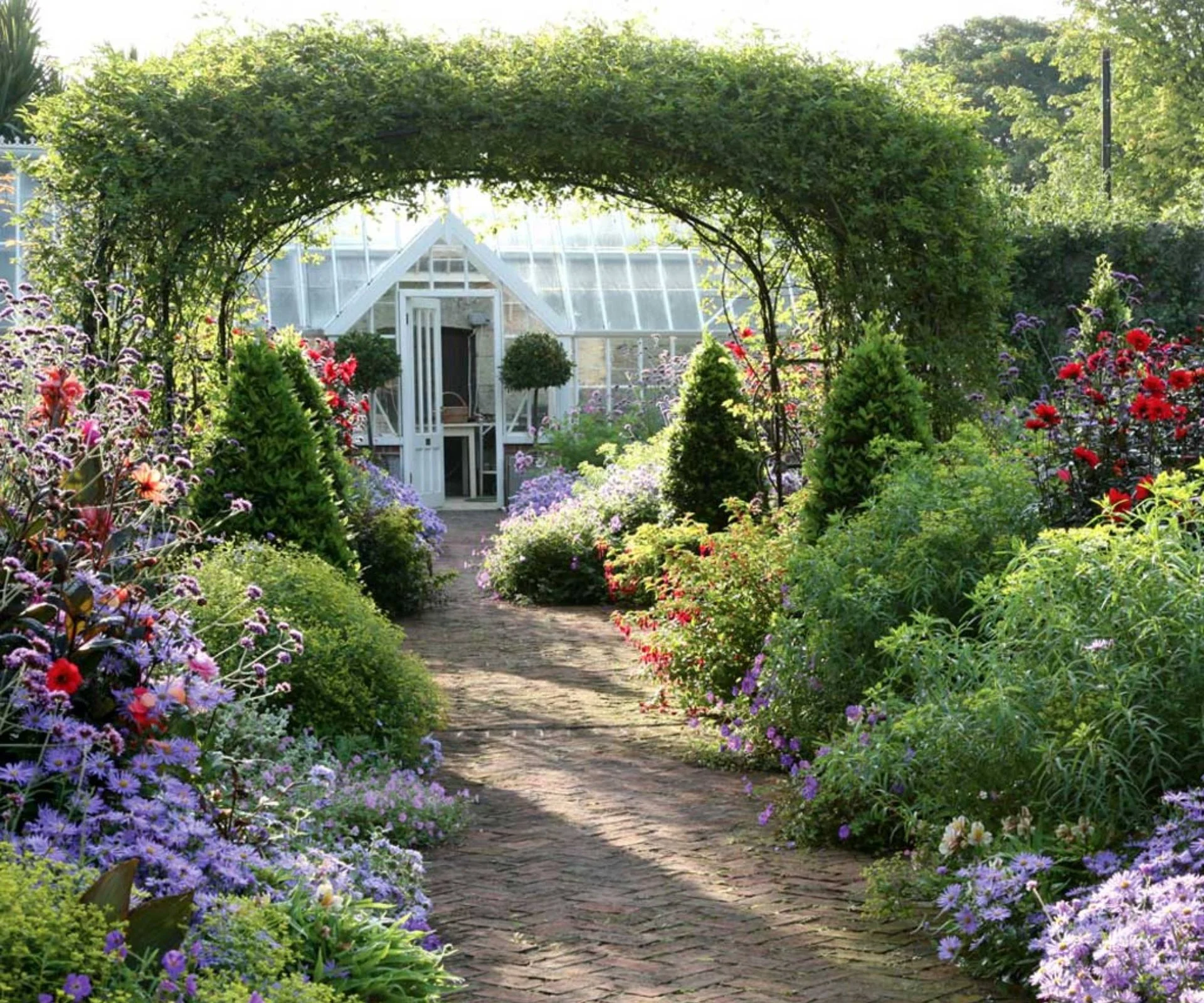 Round gazebo framing greenhouse in garden with path and borders