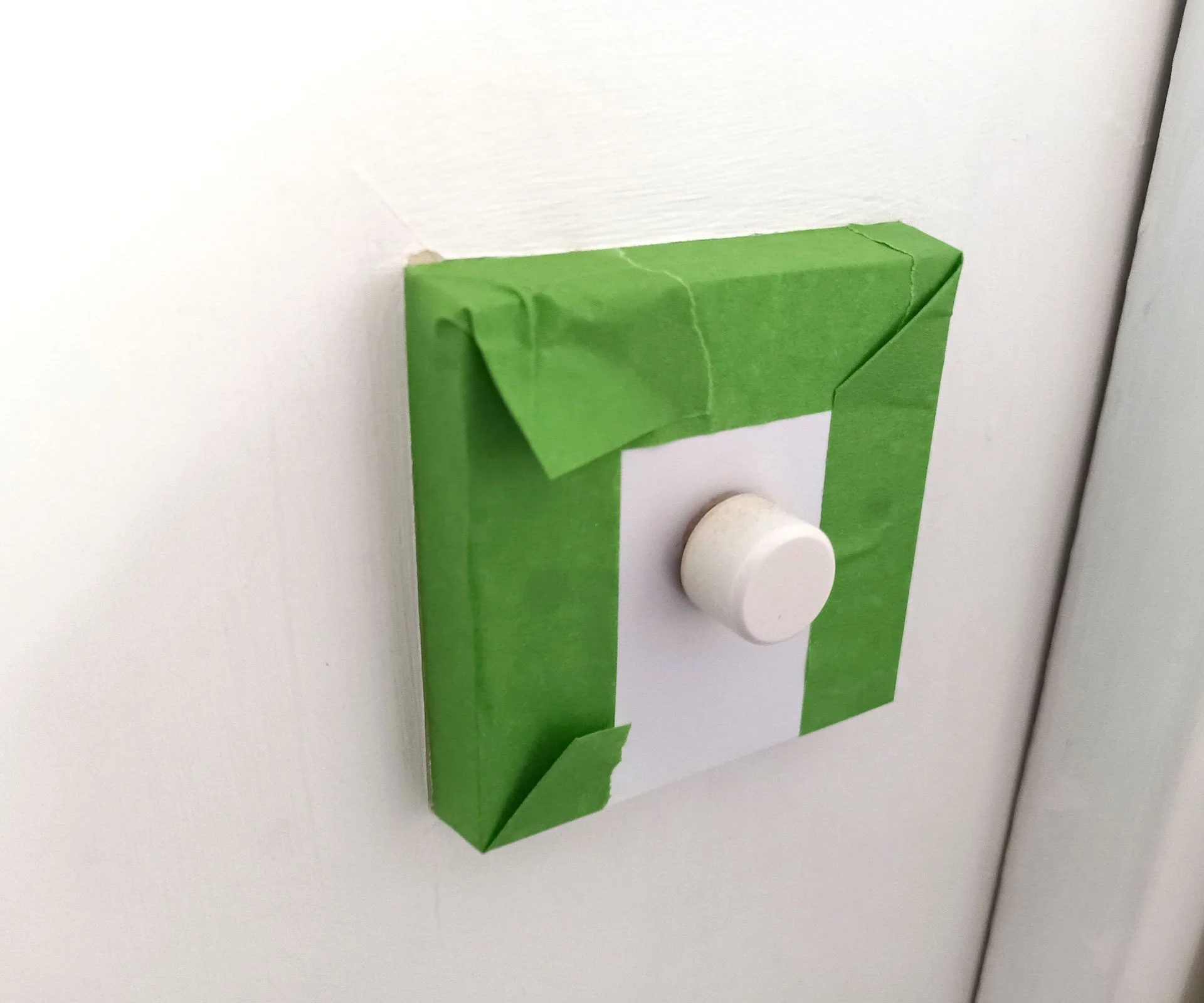 Green Frog Tape around white dimmer switch on a white wall