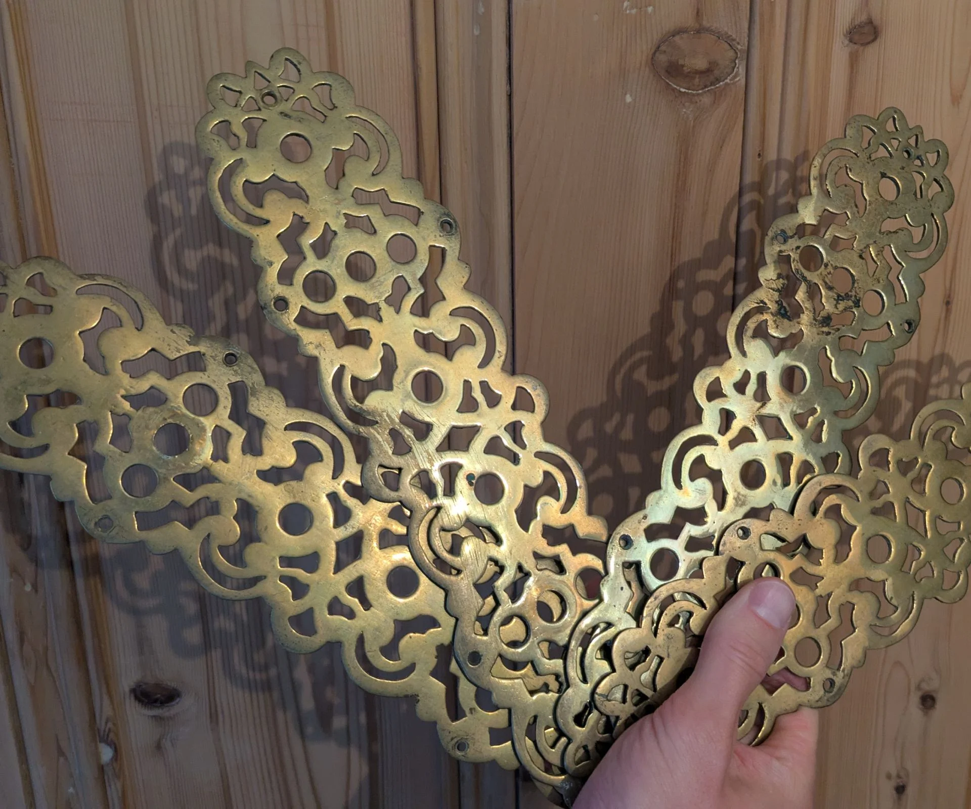 Antique brass finger plates held up against a pine door
